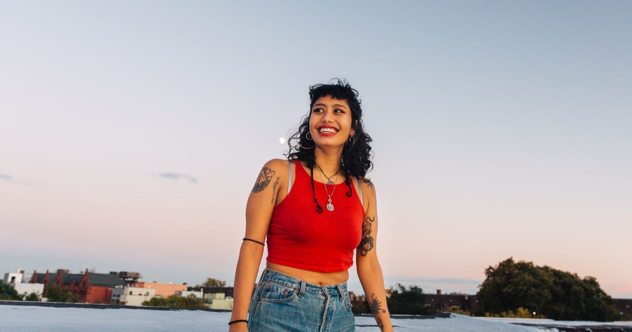 A woman smiles a large smile outside against the moonrise