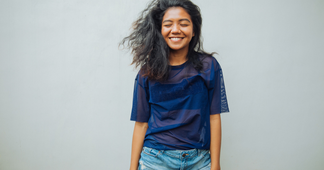 A woman smiles with her eyes closed against a blank background. 