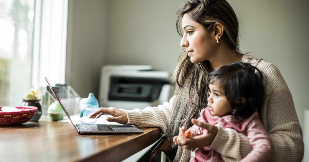 A mother holds her young child on her lap while sitting in front of a laptop. 
