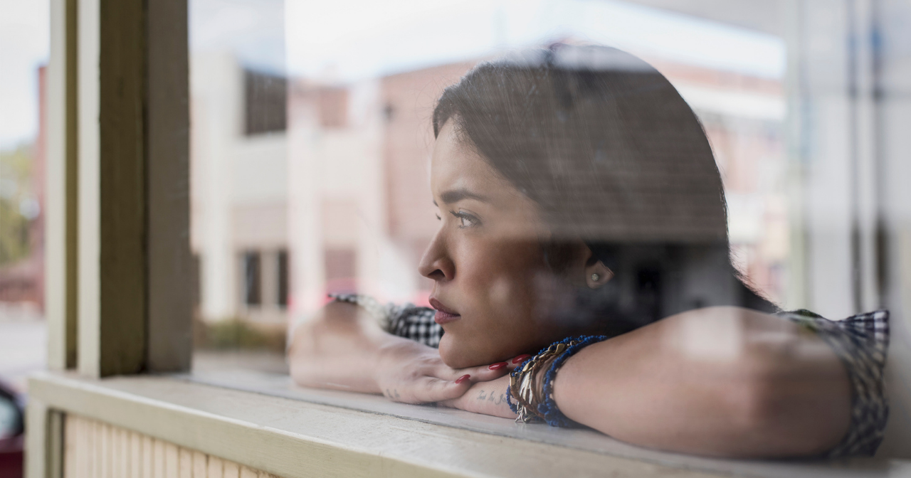 A woman looks out a window contemplatively. 