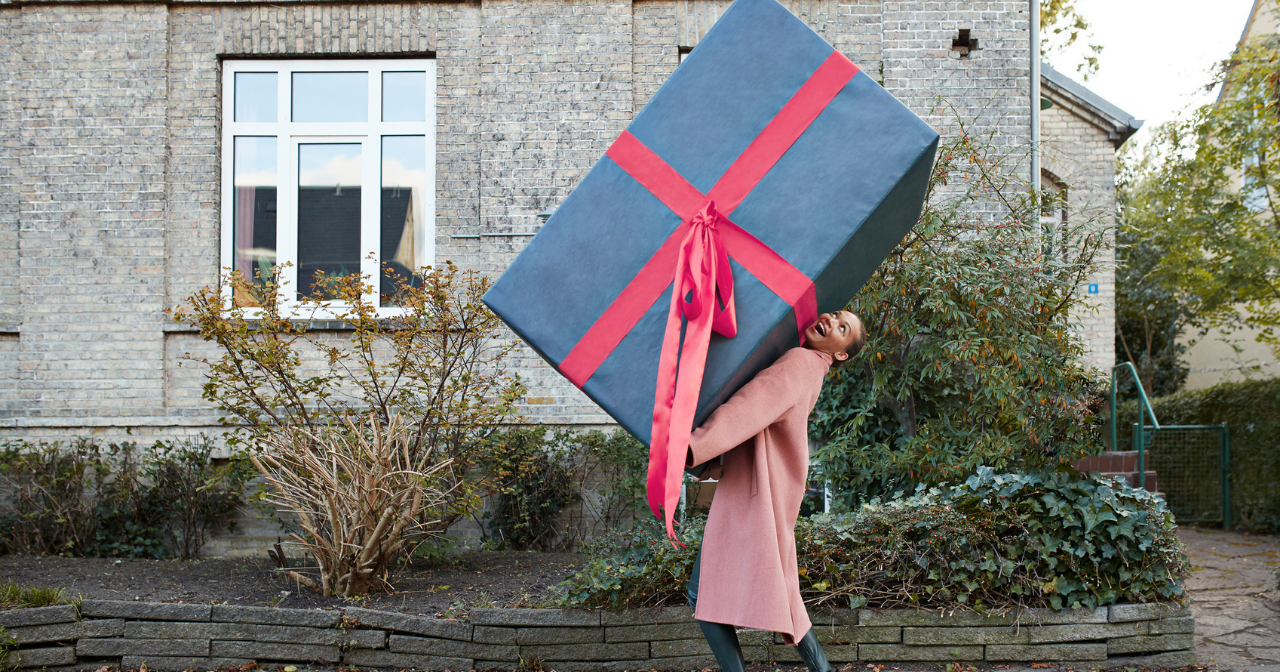 A woman walks down the street holding a comically large box. 