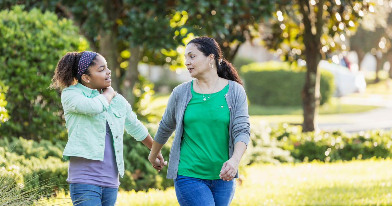 Mom and daughter walk outside hand in hand and talk. 