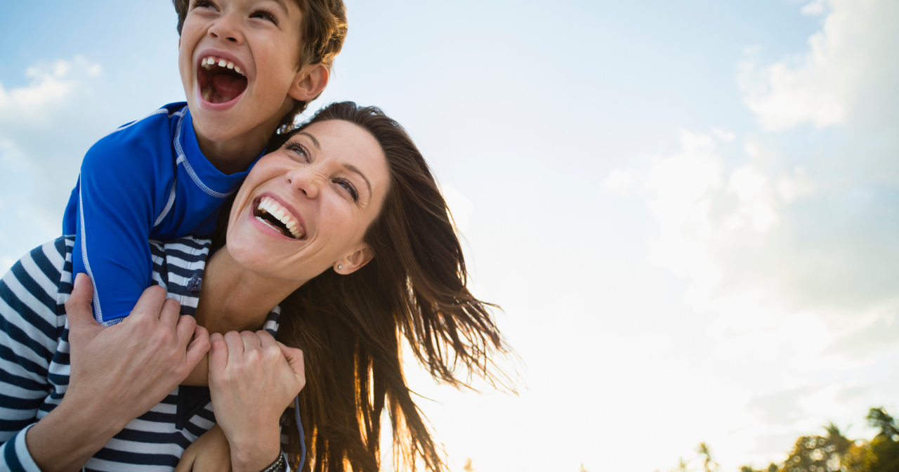 A son sits on his mom's back and the two laugh.