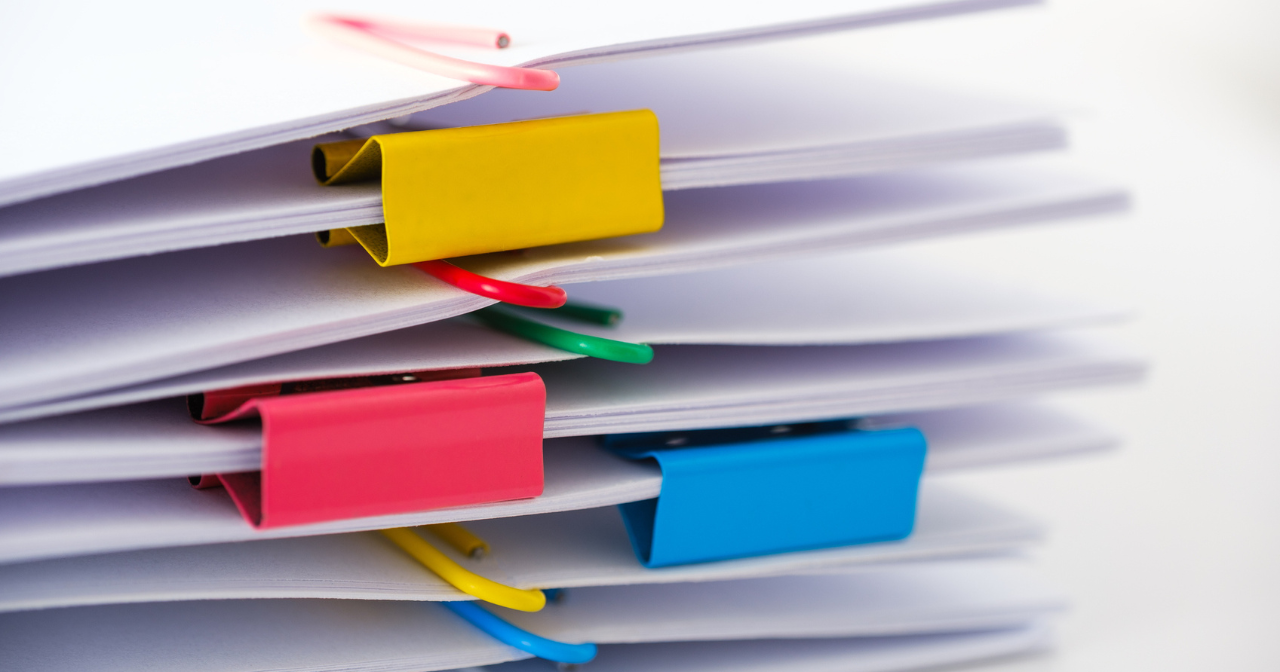 A photo of a stack of papers held together in bundles with paper and binder clips. 