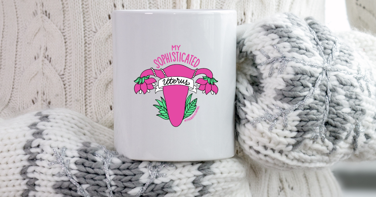 A photo of a pair of mittened hands holding a mug that says, "My sophisticated uterus"