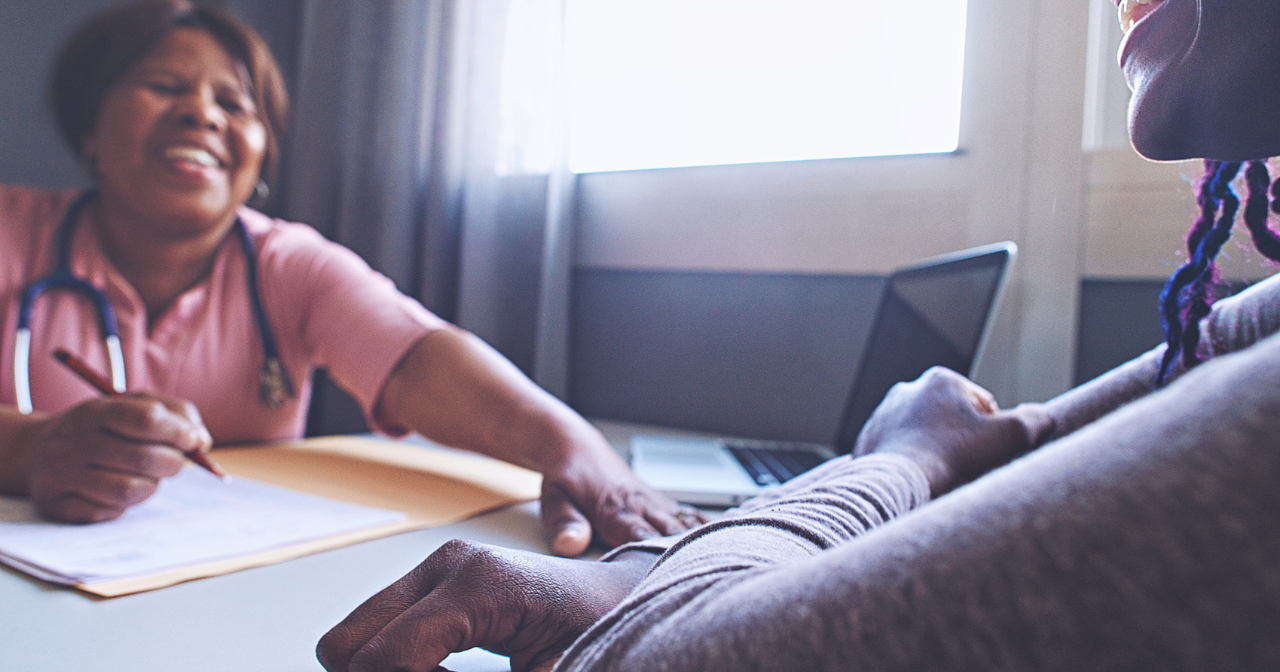 A female provider and patient laugh together while sitting across from each other at a table. 