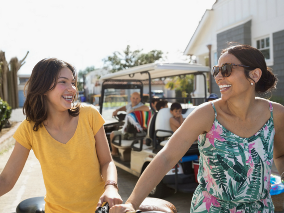 A Latina mother and daughter walk their bikes along a street
