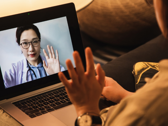 A provider waves at a patient through a laptop screen. 