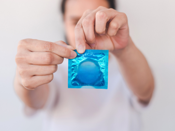 An out of focus woman holds a condom in its wrapped and begins to open it. 