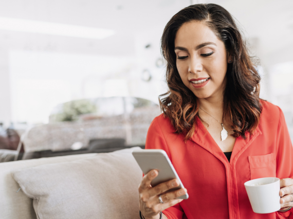 A woman sits on her sofa with a cup of coffee and her phone. 