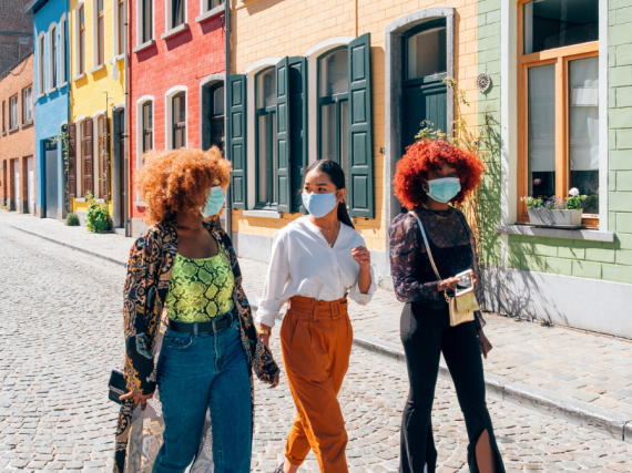 Three friends wearing masks walk down the street and laugh. 