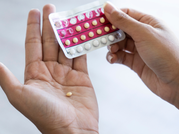 A photo of a pair of hands, one holding a packet of birth control pills and the other with a single pill resting in the palm. 