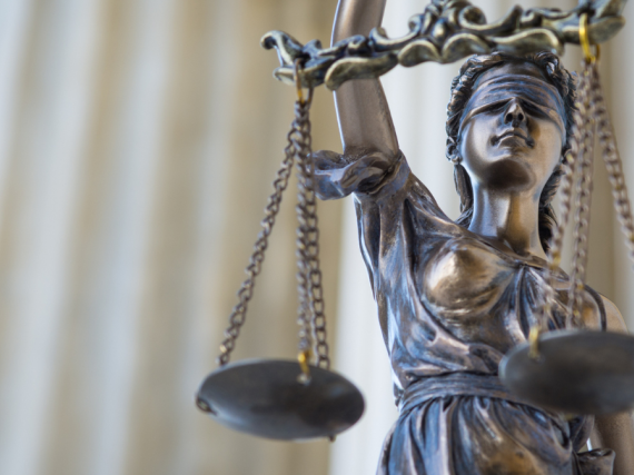 A photo of the statue of blind justice holding scales against the background of the Supreme Court's columns. 