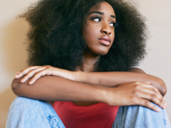 A photo of a Black woman sitting on the floor with her arms crossed, looking concerned. 
