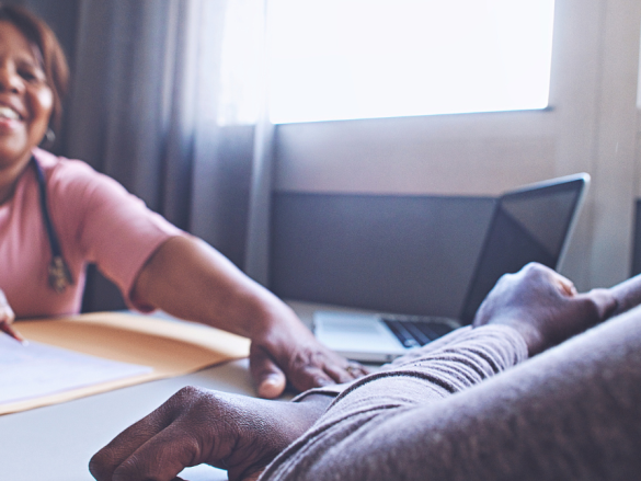 A female provider and patient laugh together while sitting across from each other at a table. 